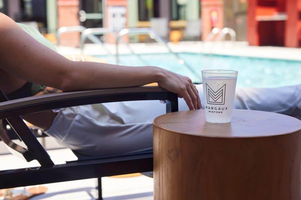 Resident lounging by pool with Margaux Midtown branded cup